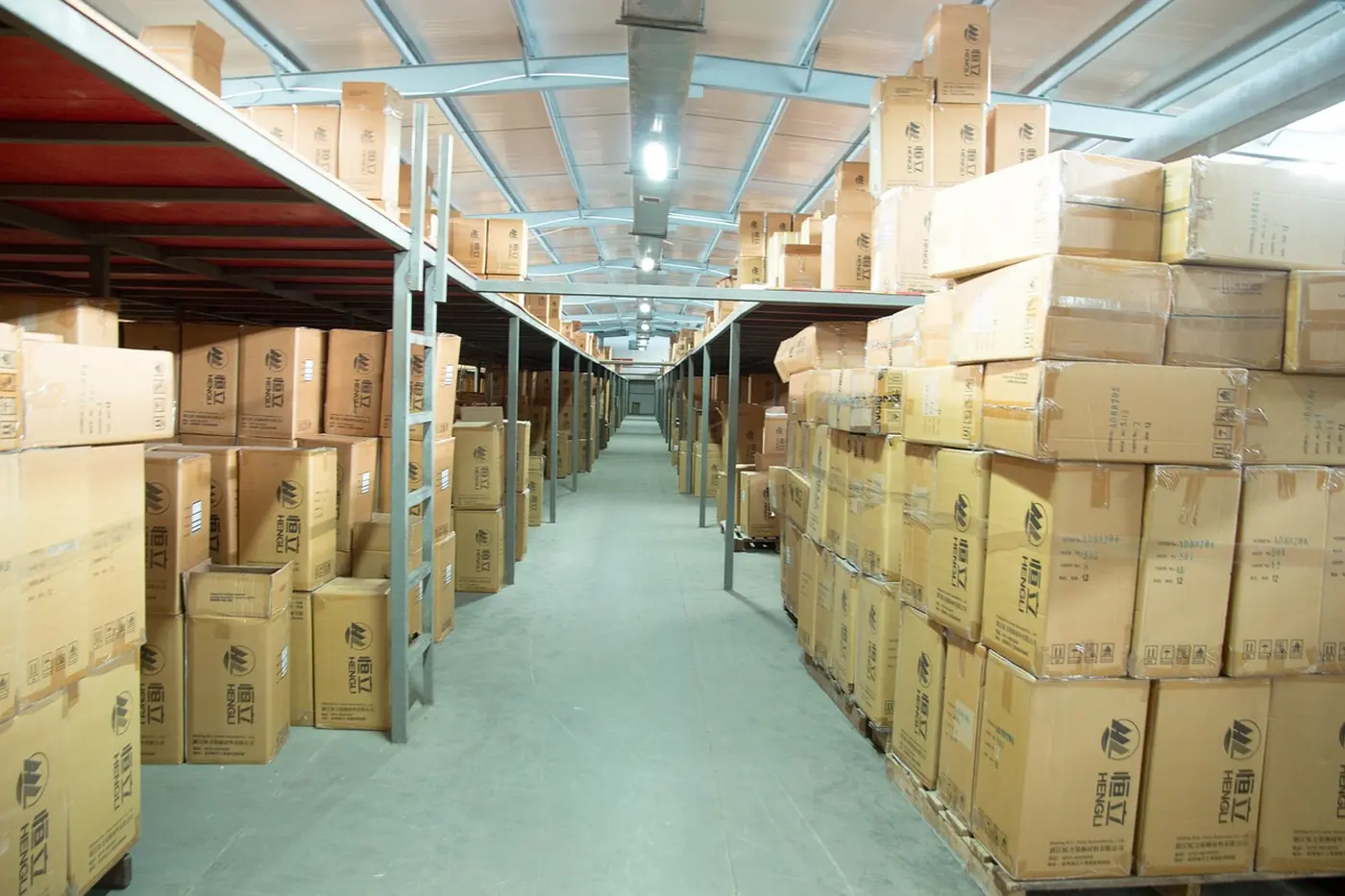 Long warehouse aisle between stacks of cardboard cartons on metal shelving and pallets